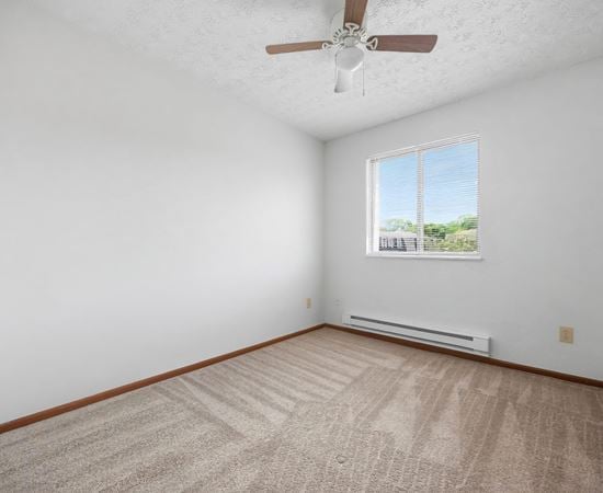 A room with a ceiling fan and a window with a view of trees and a fence outside.